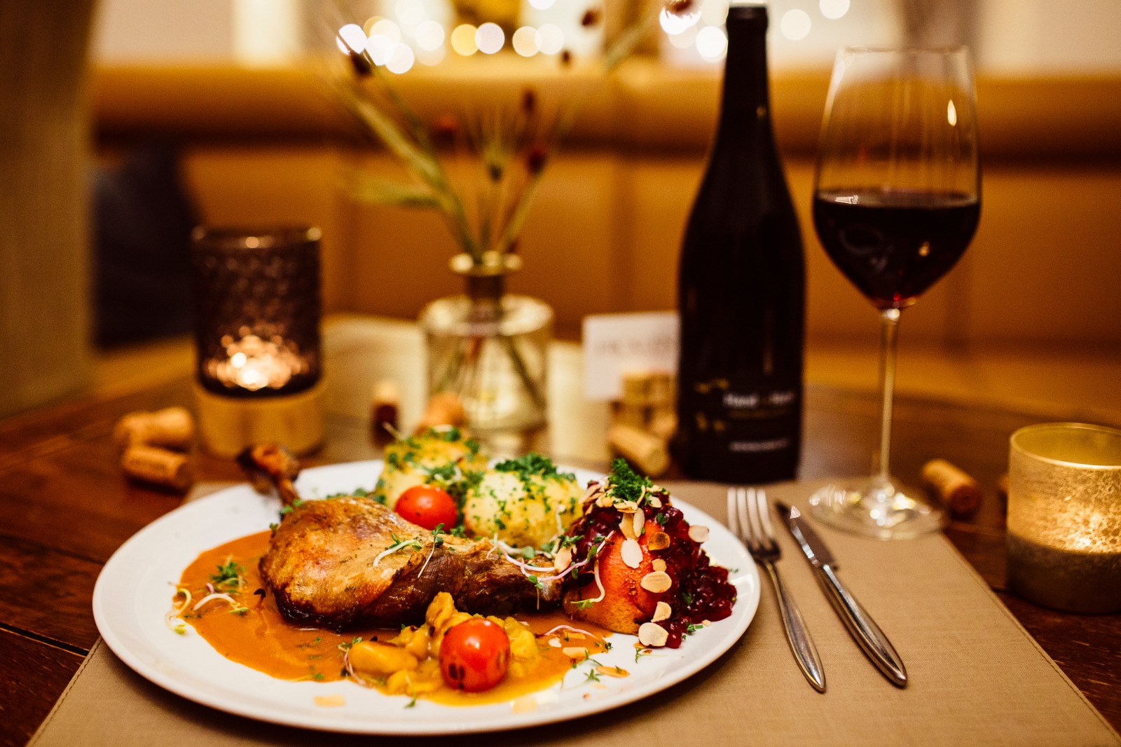 Gänsekeule mit Kartoffelklößen, Apfelrotkohl und Bratapfel auf dem Teller, dazu ein Glas Rotwein